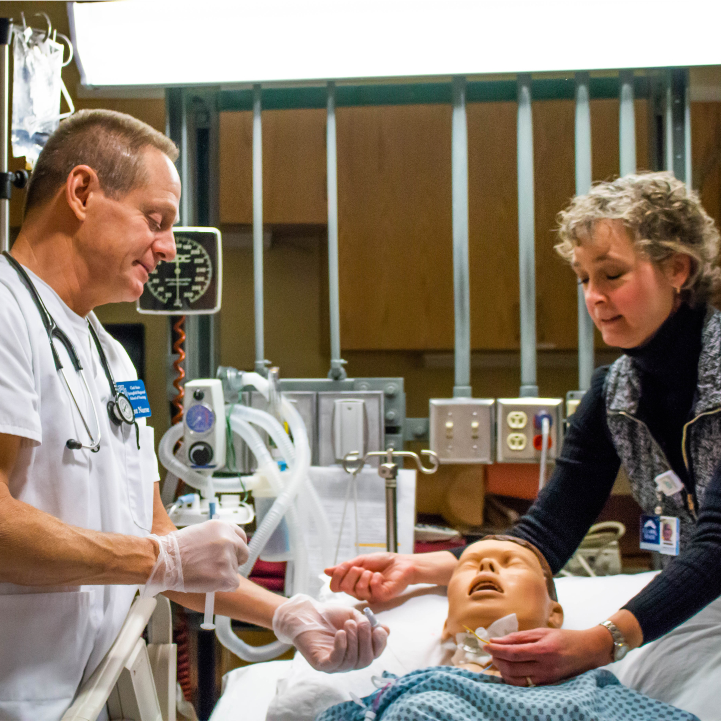 Male and female nurse practice on mannequin patient in bed.