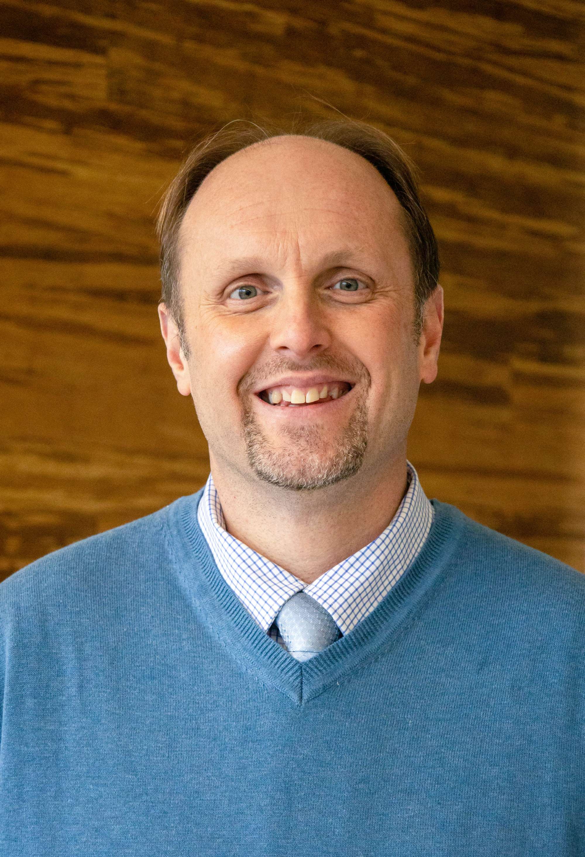 Dr. Dawayne Kirkman headshot in blue sweater with white collar and blue tie.