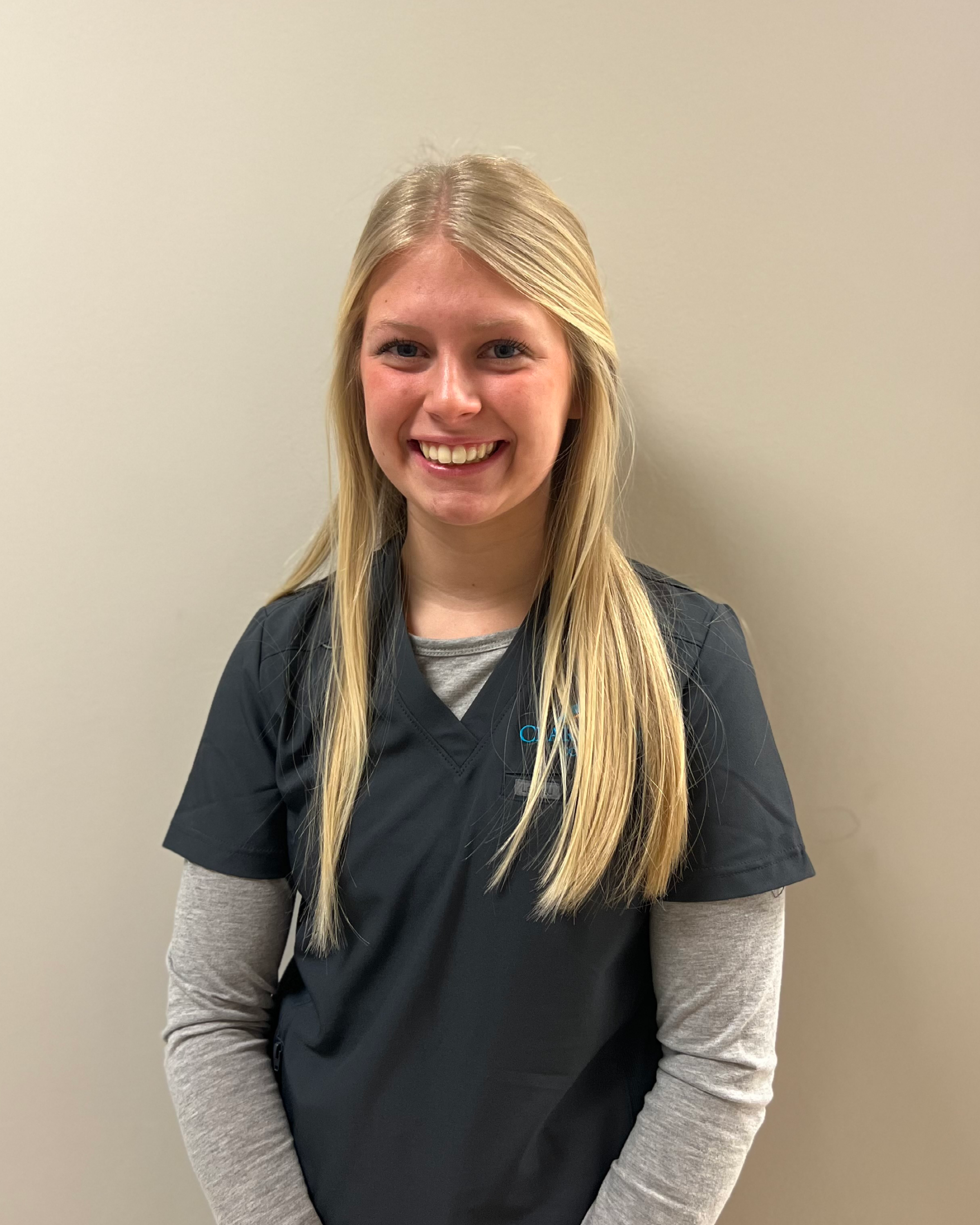 Smiling female student with long blonde hair wearing blue medical scrubs.