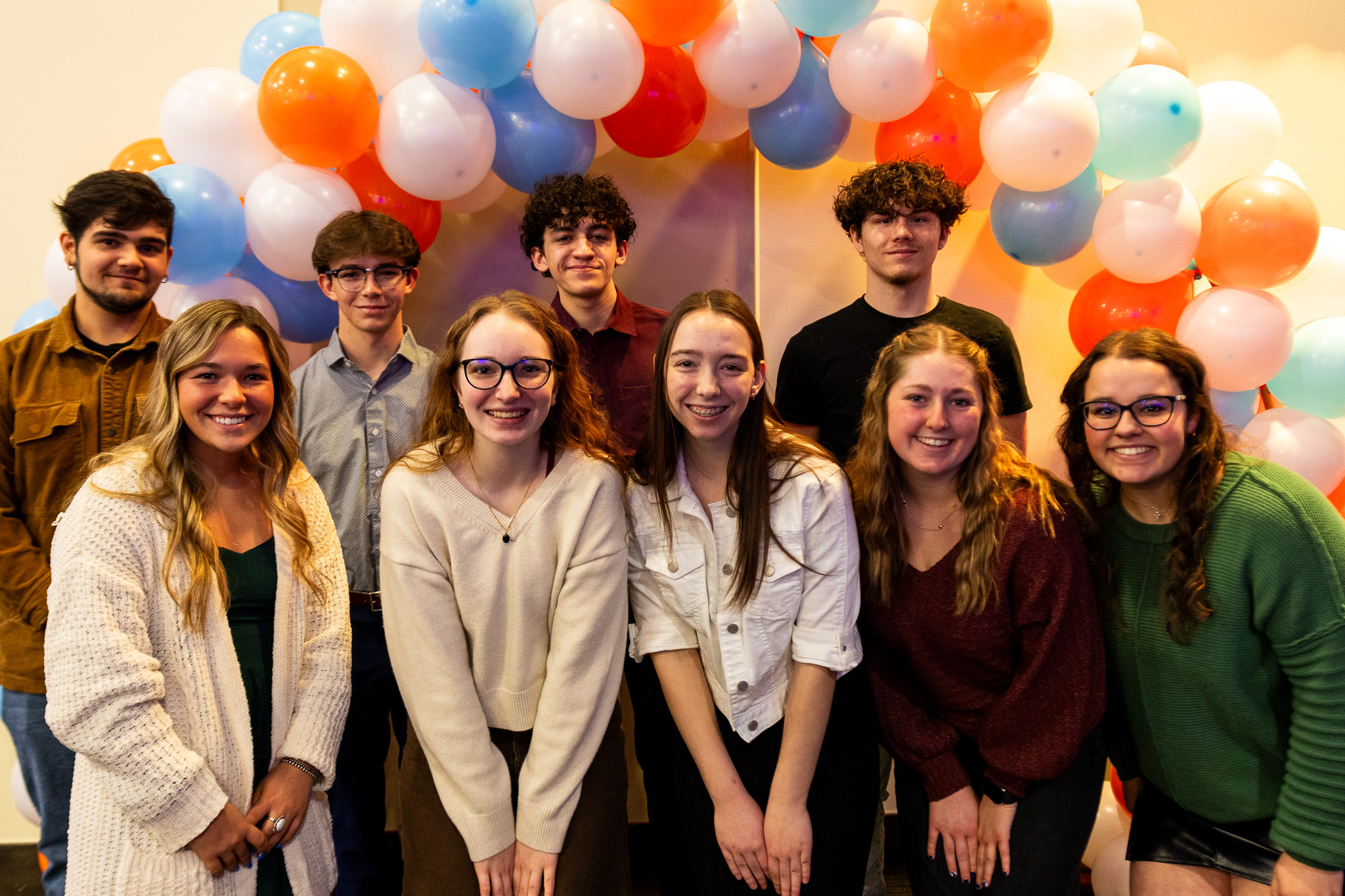 Nine high school students standing underneath a balloon arch for a group photo.